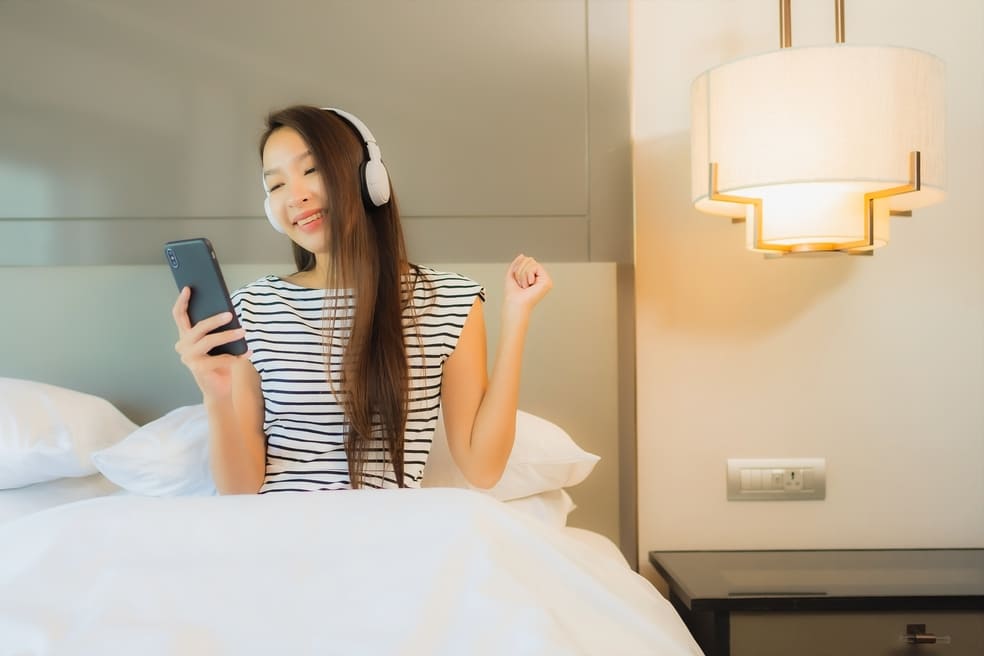 portrait-beautiful-young-asian-woman-use-smart-mobile-phone-with-headphone-listen-music-bedroom-interior