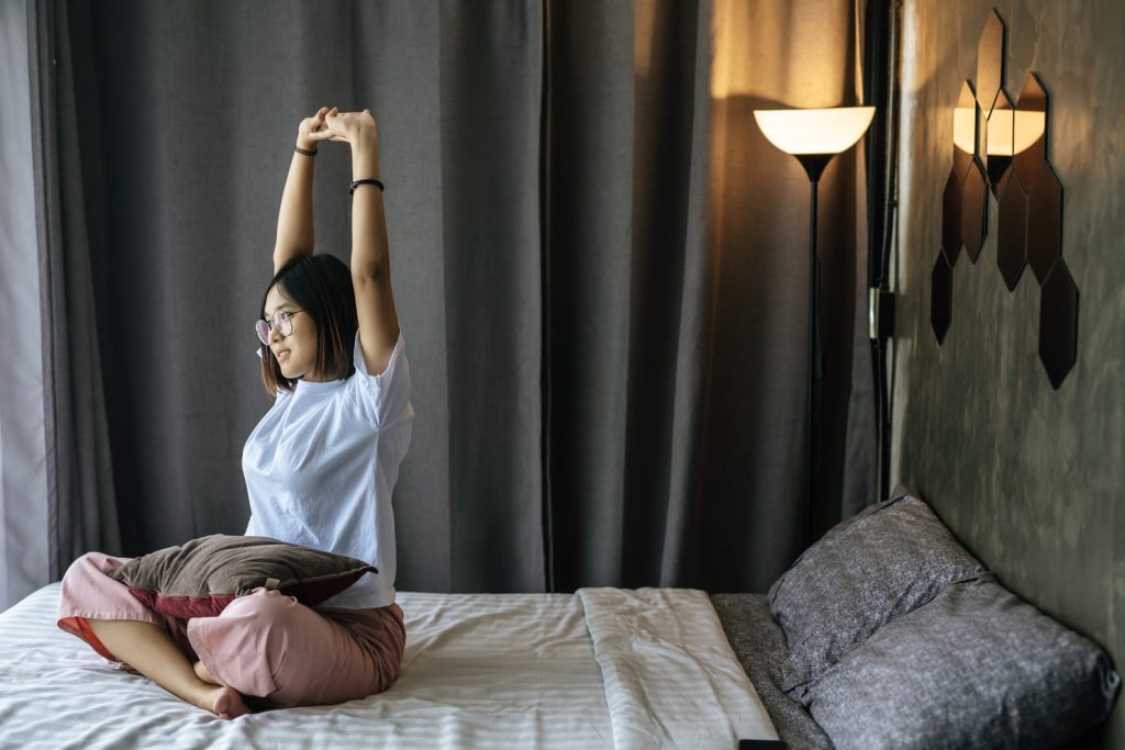 woman-white-shirt-sitting-bed-raising-both-arms